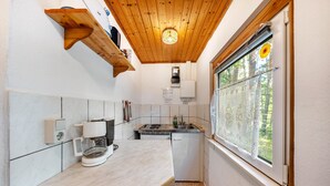 Une cuisine compacte avec un plafond en bois, une machine à café, un évier et une fenêtre donnant sur les arbres.