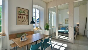 A modern interior with a wooden dining table, teal chairs, a black pendant light, and a large window.