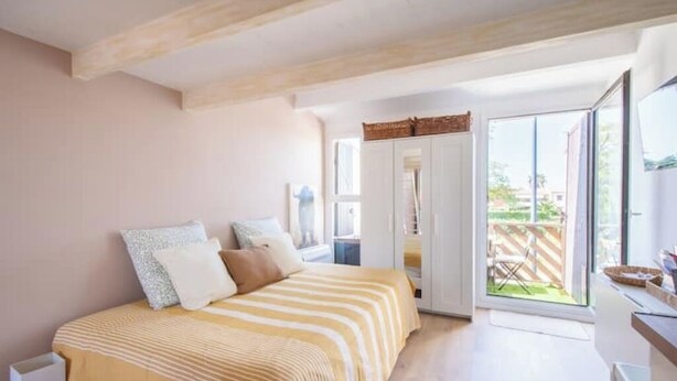 Ein Schlafzimmer mit einem Bett, einer Schiebetür zu einem Balkon und Blick ins Freie.