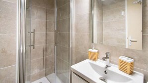 Ein modernes Badezimmer mit einer gläsernen Duschkabine, einem weißen Waschbecken mit Holzseifenablagen und einem großen Spiegel.