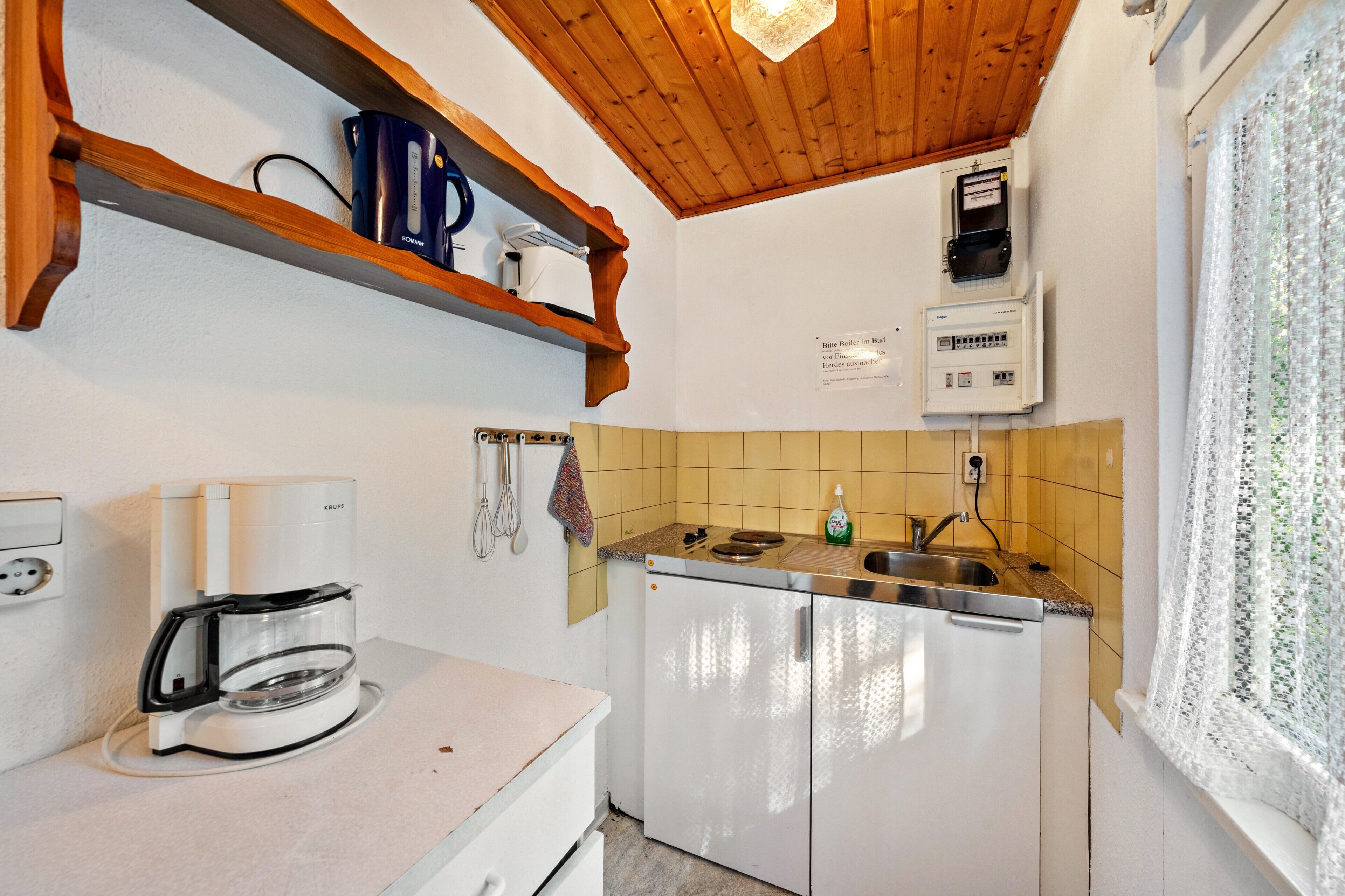 A kitchen with a coffee maker, a refrigerator, a sink, and wooden shelves.