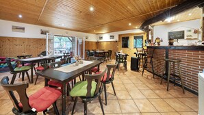 A restaurant with wooden ceiling, multiple tables and chairs, a bar area, and a chalkboard menu.