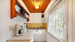 A compact kitchen with a wooden ceiling, a window with lace curtains, and a built-in coffee maker.
