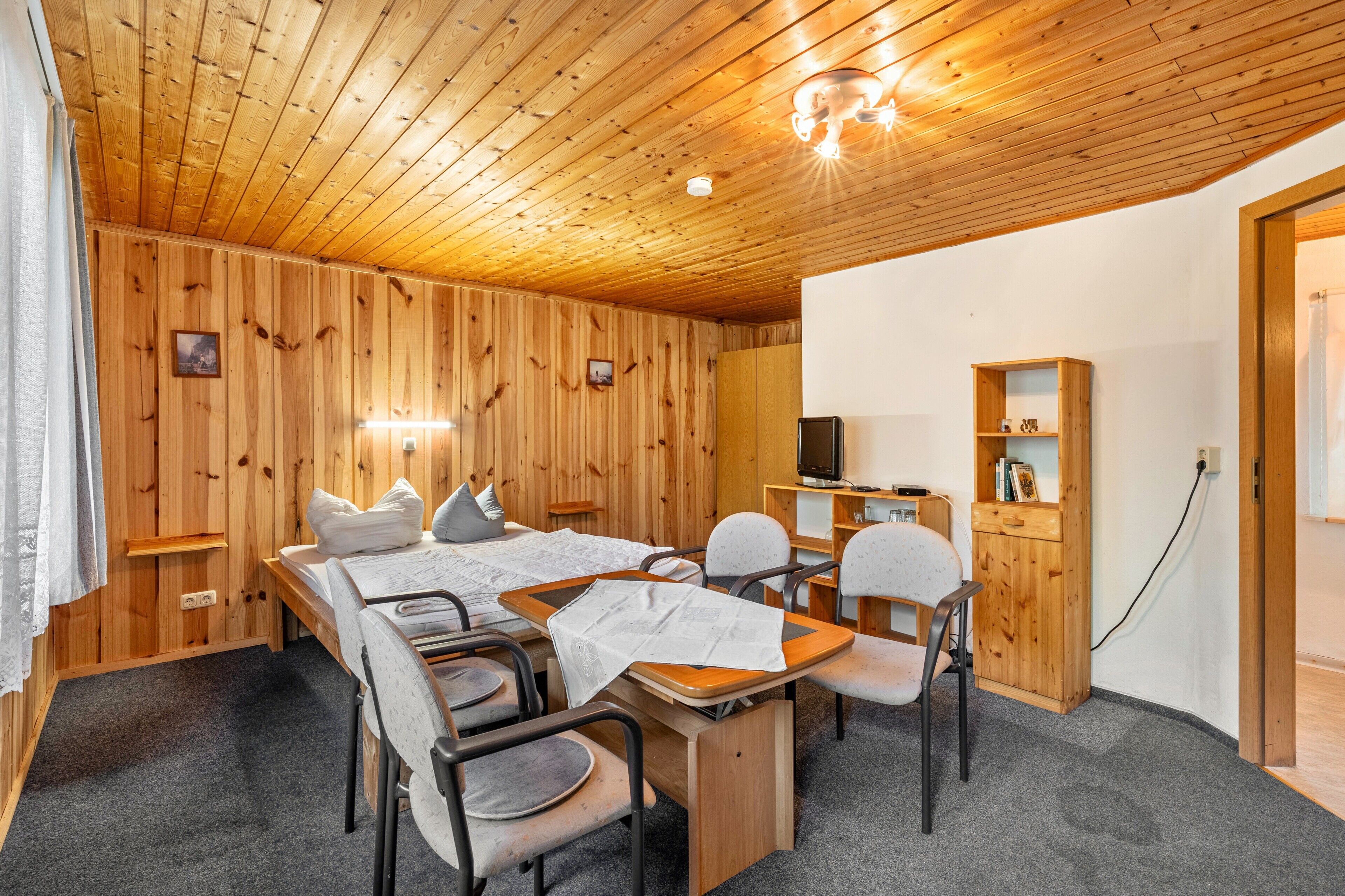 Une pièce aux murs lambrés, avec un lit, un bureau et des chaises.