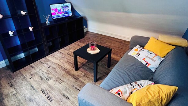 Uma sala de estar moderna com um sofá cinzento, uma mesa de centro preta e uma televisão sobre um suporte preto.