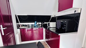 Uma cozinha compacta com armários vermelhos, bancada preta e micro-ondas.