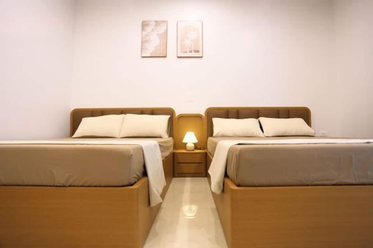 A hotel room with two beds, a nightstand with a lamp, and two wall art pieces.