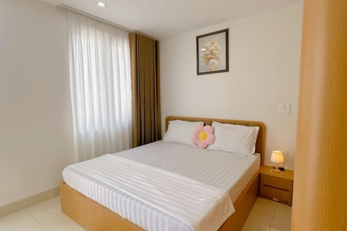 Een net opgemaakt bed met een kussen, een bedlampje en een ingelijste foto aan de muur.