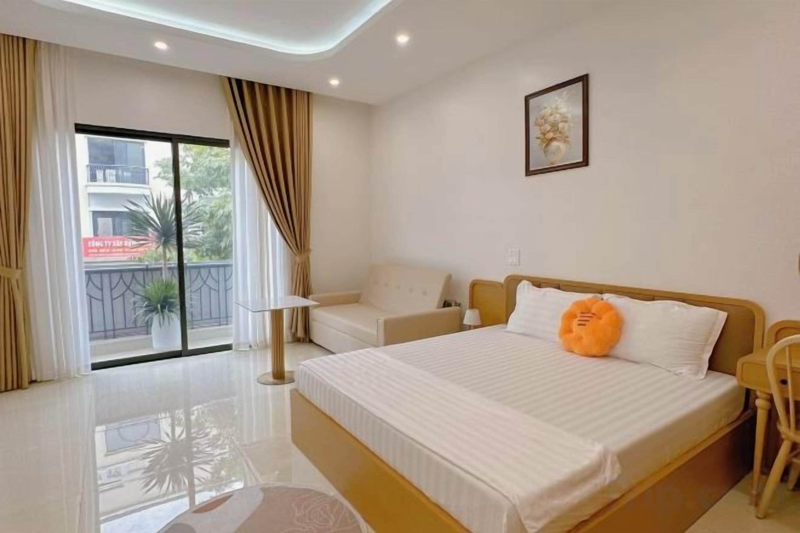 A hotel room with a large bed, a sofa, a chair, a balcony with curtains, and a door to the outside.