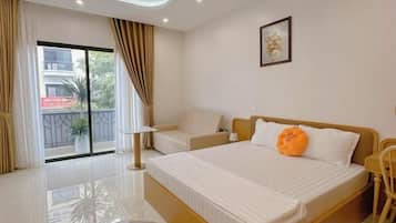 A hotel room with a large bed, a sofa, a chair, a balcony with curtains, and a door to the outside.