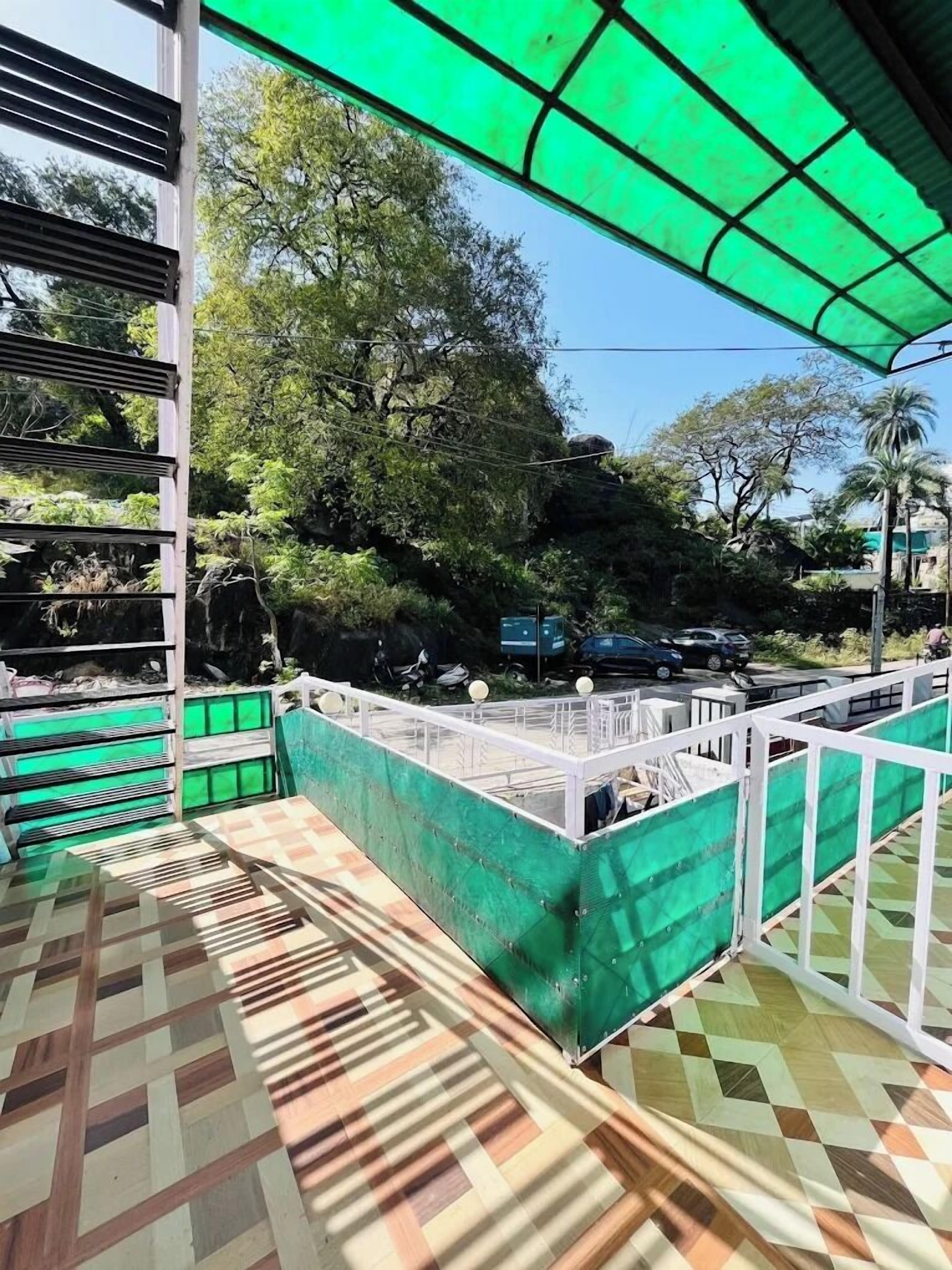 A covered outdoor area with a patterned floor, a green fence, and trees in the background.