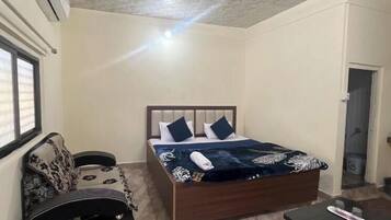 A bedroom with a bed, a sofa, a small table, and a ceiling fan.