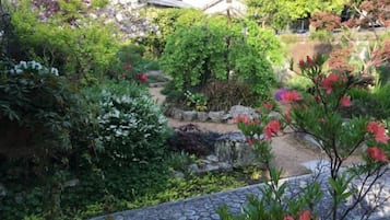 Un jardí amb un camí de pedra, diverses plantes i un edifici tradicional al fons.