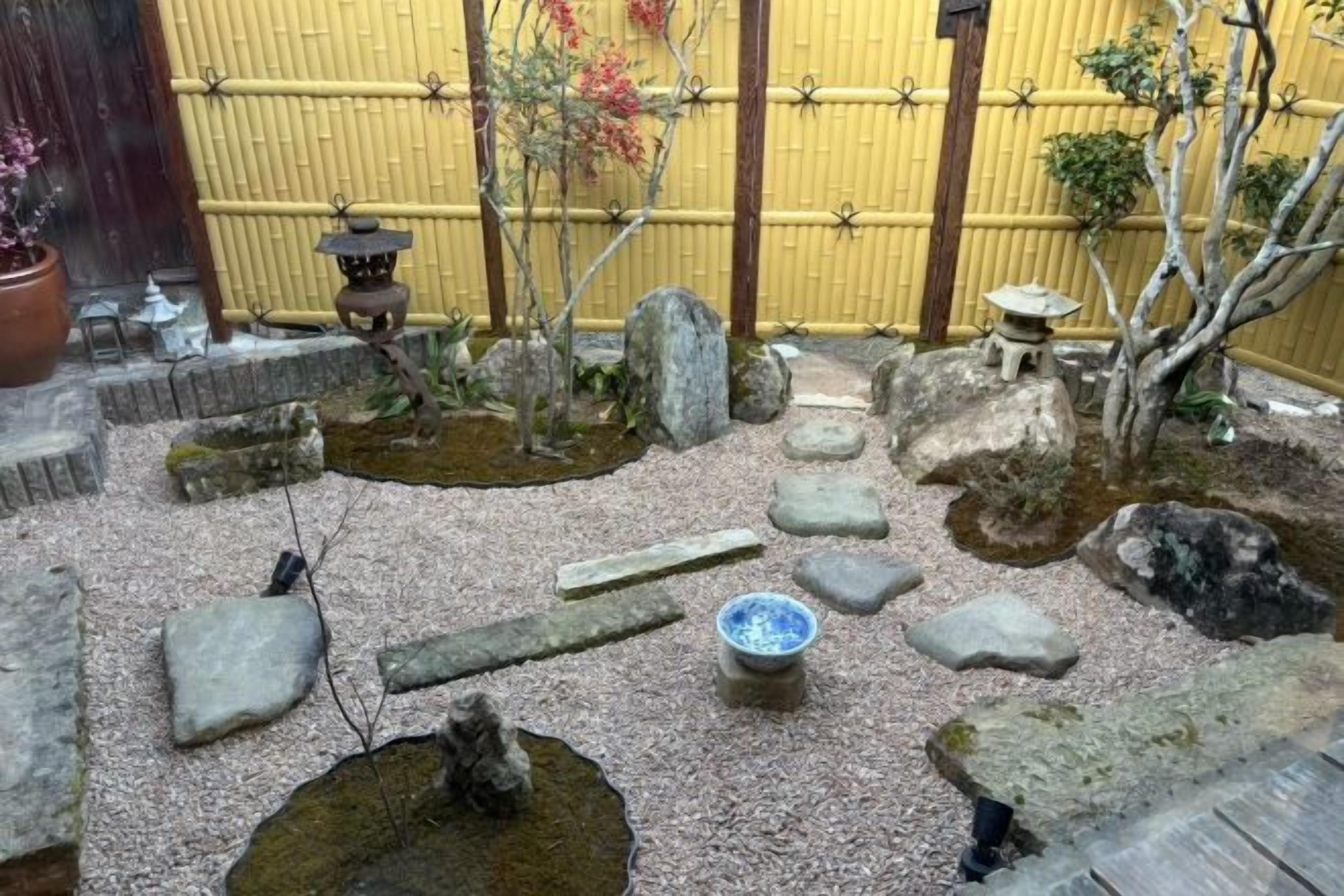 Un jardin japonais traditionnel agrémenté d’une lanterne en pierre, d’un petit étang et de diverses roches et plantes.