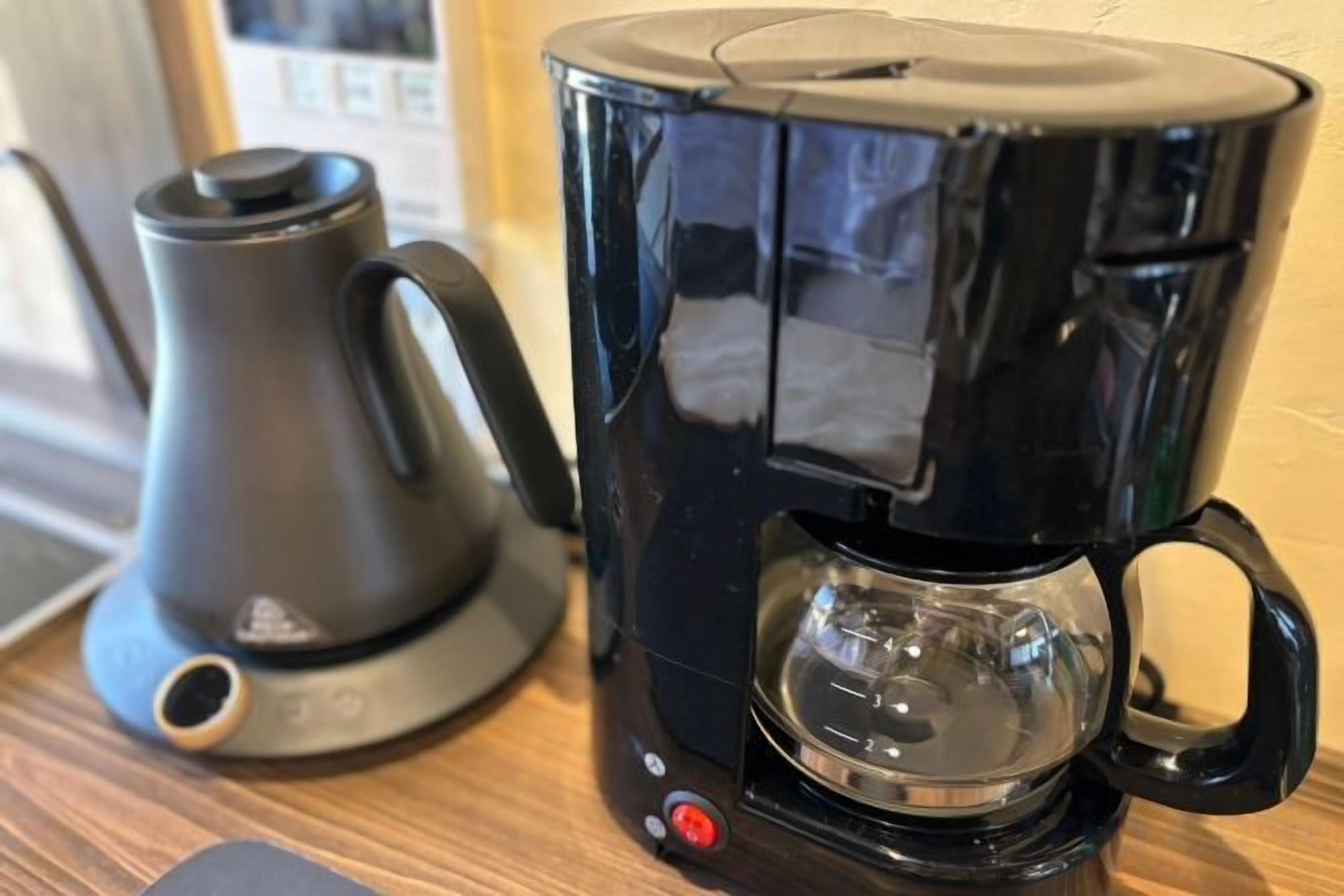 A black coffee maker with a transparent water reservoir and a separate electric kettle on a wooden surface.