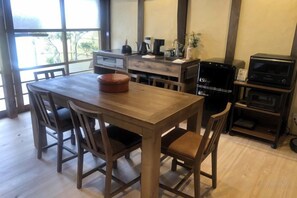 Ein Holztisch mit Stühlen, eine Kaffeemaschine und ein Fernseher in einem Zimmer mit großen Fenstern.