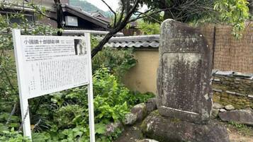 A stone monument with a sign in front of it, surrounded by greenery and a traditional building in the background.