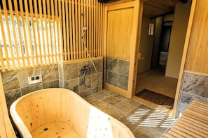Une baignoire en bois dans une salle de bain aux murs carrelés et dotée d’une porte en bois.