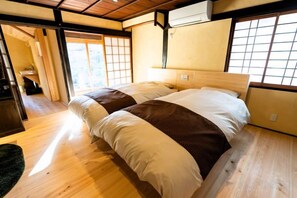 Una habitación tradicional japonesa con suelo de madera, una cama con cabecera y un puertas correderas que dan a otra habitación.