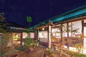 Un bâtiment traditionnel japonais doté d’une entrée couverte, d’un chemin en pierre et de plantes en pot.