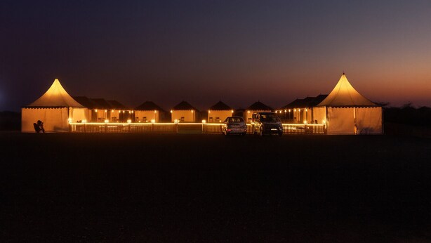 A row of tents with a central walkway, each tent with a peaked roof and a small porch. - Stayguru Patgar Tent (Bhuj)
