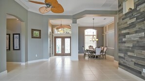 Ein geräumiges Wohnzimmer mit Deckenventilator, einem Essbereich mit einer Chandelier und einer Wand als Akzent mit Steinplatten.