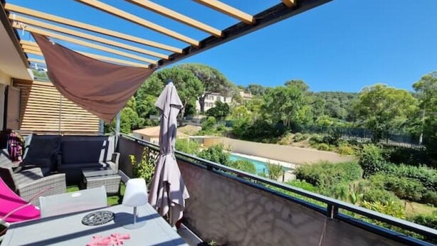 Een balkon met buitenmeubilair, uitzicht op een zwembad en omliggend groen.