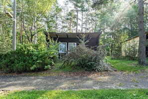 Un chalet isolé, doté d’un petit porche, entouré d’une forêt dense.