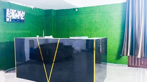 A reception desk with a black surface and yellow accents, set against a green wall with a mounted television. - Roomshala Hotel Jagannath (New Delhi)