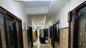 A hotel corridor with tiled floors, wooden doors, and a reception desk in the distance. - Roomshala Hotel Jagannath (New Delhi)