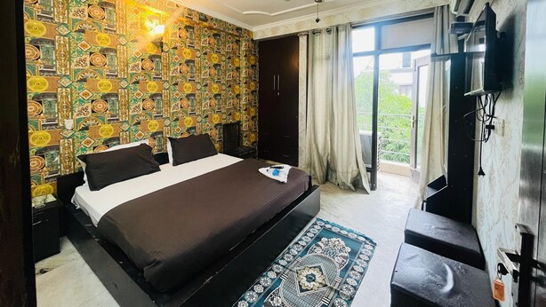 A hotel room with a bed, a ceiling fan, a TV, and a large window with curtains. - Roomshala Hotel Jagannath (New Delhi)