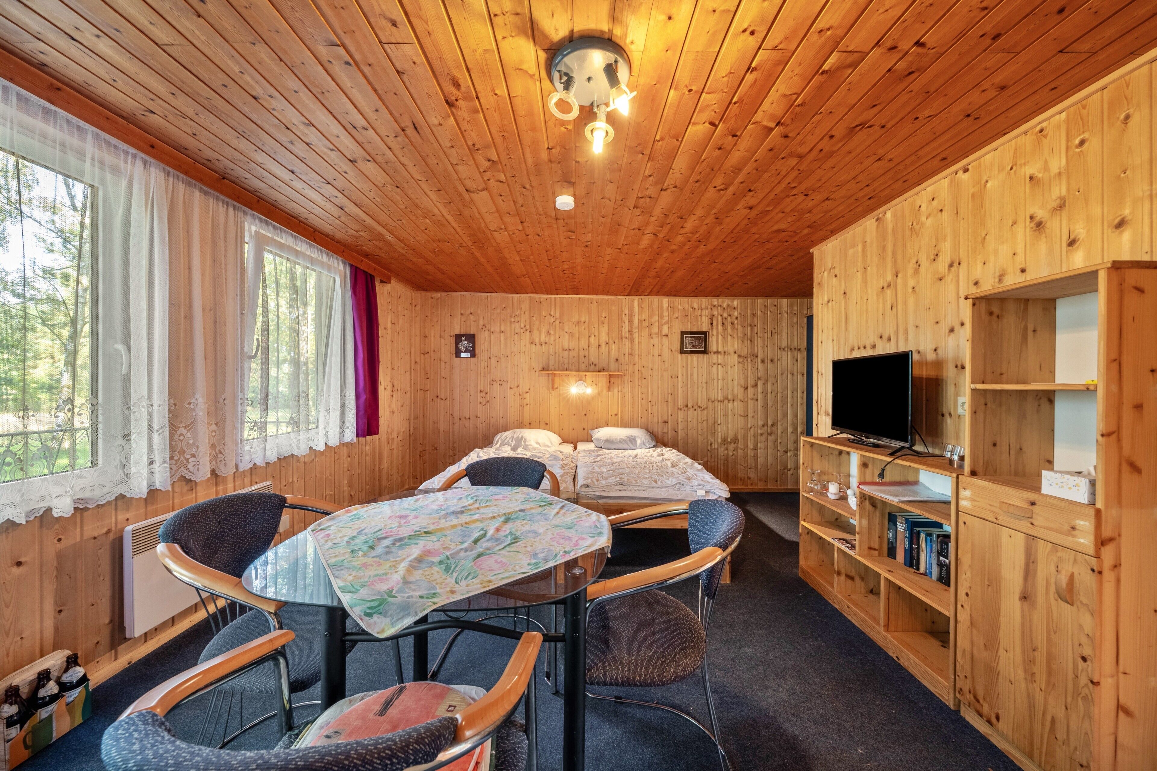 A wooden cabin with a dining table, chairs, a TV, and a bookshelf.