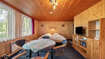 A wooden cabin with a dining table, chairs, a TV, and a bookshelf.