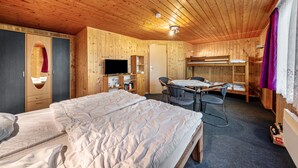 Habitación con paneles de madera, una cama, un escritorio, una silla, un televisor y una litera.