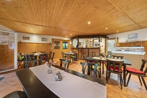 A restaurant with wooden ceiling and walls, tables with chairs, and a counter with a display case.