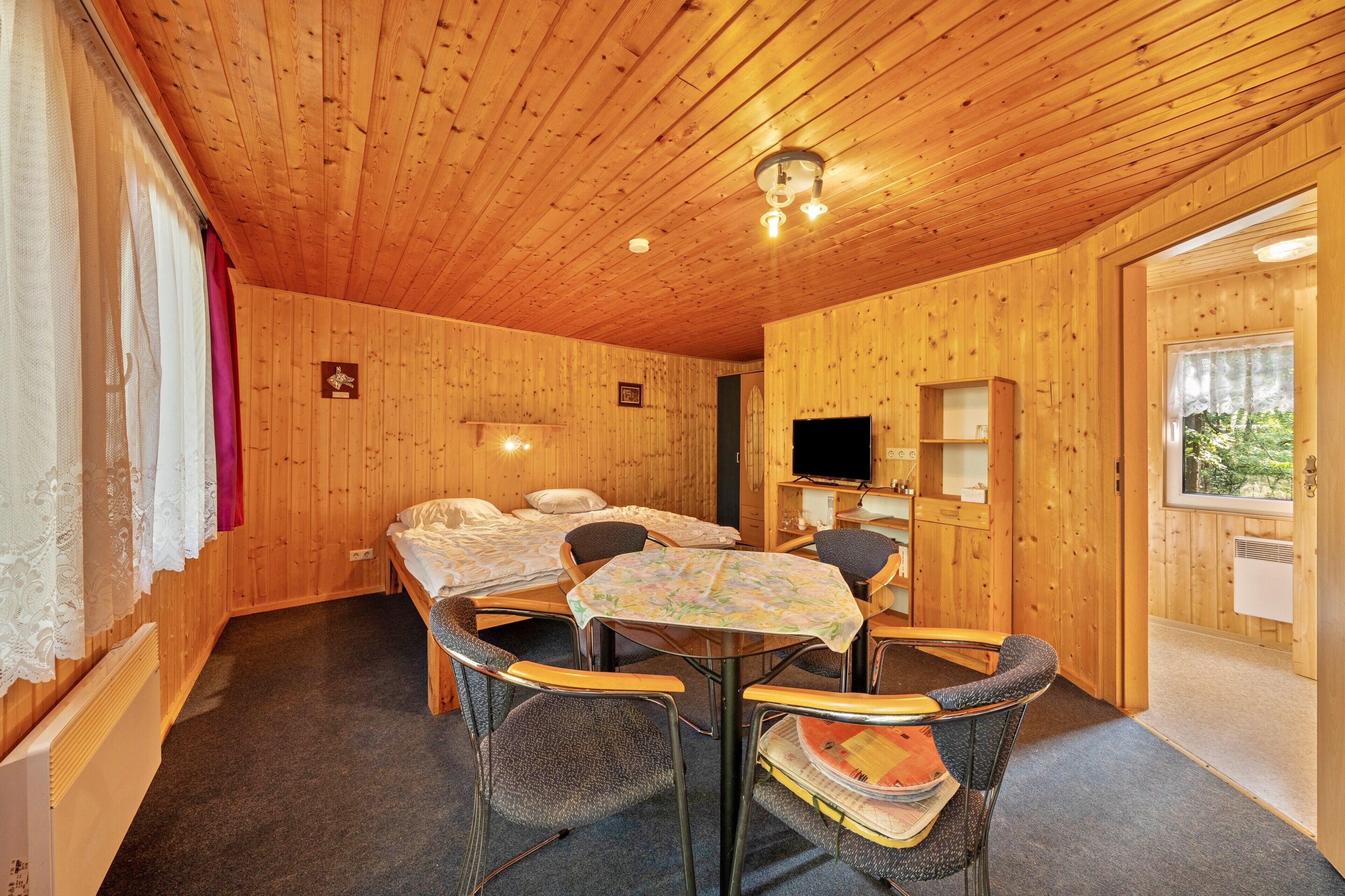 Una habitación de cabaña de madera con una cama, una mesa con sillas, un televisor y una ventana.