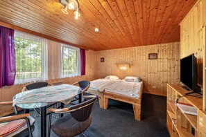 A wooden cabin with a bed, a TV, a table with chairs, and a window with curtains.