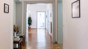 A hallway with wooden flooring, a hanging light fixture, and framed pictures on the walls.