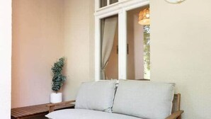 A wooden bench and a light-colored sofa in a corner with a window and a wall-mounted light fixture.