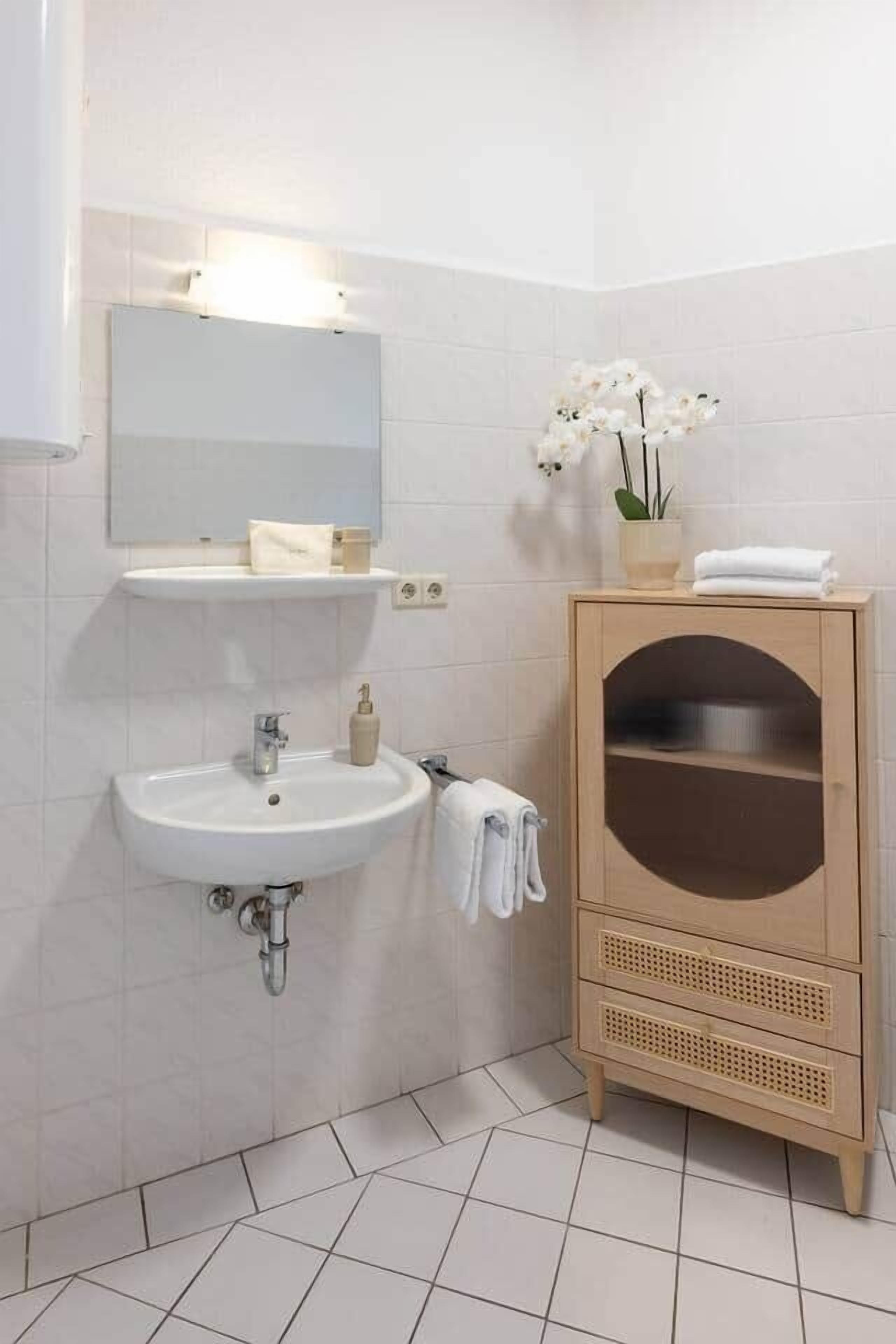 Une salle de bain avec un lavabo blanc, un miroir et un meuble en bois orné d’une découpe décorative.