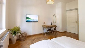 A bedroom with a bed, a desk, a television, a mirror, and a door. - Cozy Guesthouse at Winckel (Stendal)