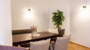 A dining area with a wooden table, four chairs, a potted plant, and two wall-mounted lights. - Cozy Guesthouse at Winckel (Stendal)
