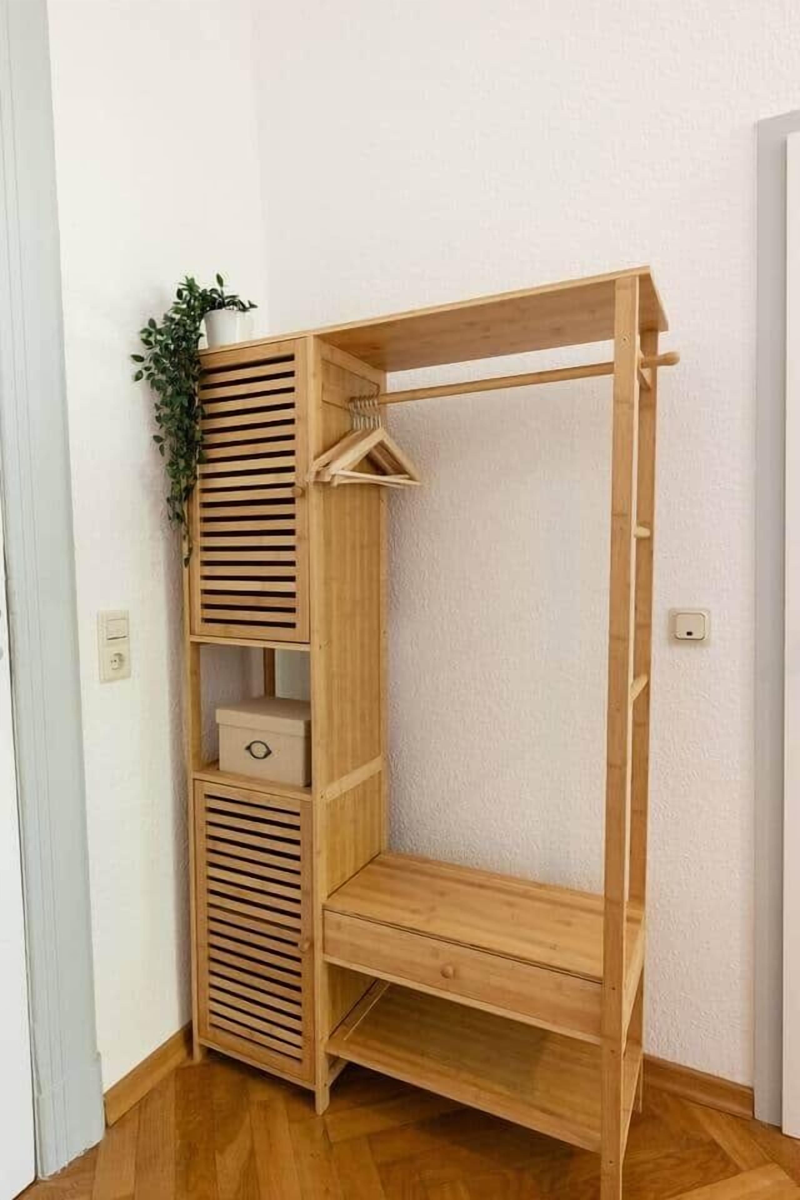 A wooden wardrobe with multiple shelves and a hanging rod, a small plant on top, and a drawer unit.