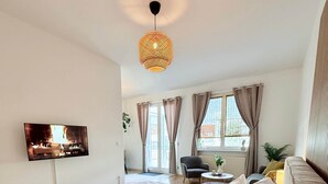 A bedroom with a bed, a TV mounted on the wall, a window with curtains, and a hanging light fixture. - Altstadt Studio - Hygge im Hoock (Stendal)