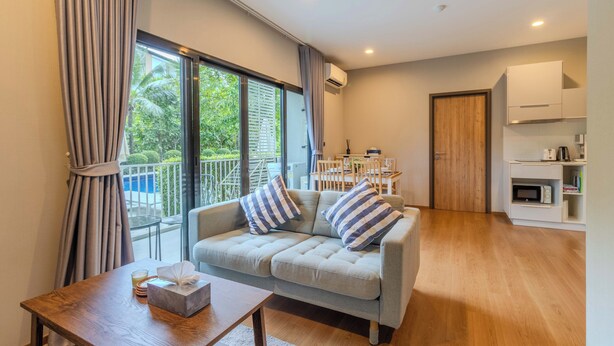 Een moderne woonkamer met een grijze bank, gestreepte kussens, een houten salontafel en een eethoek op de achtergrond.