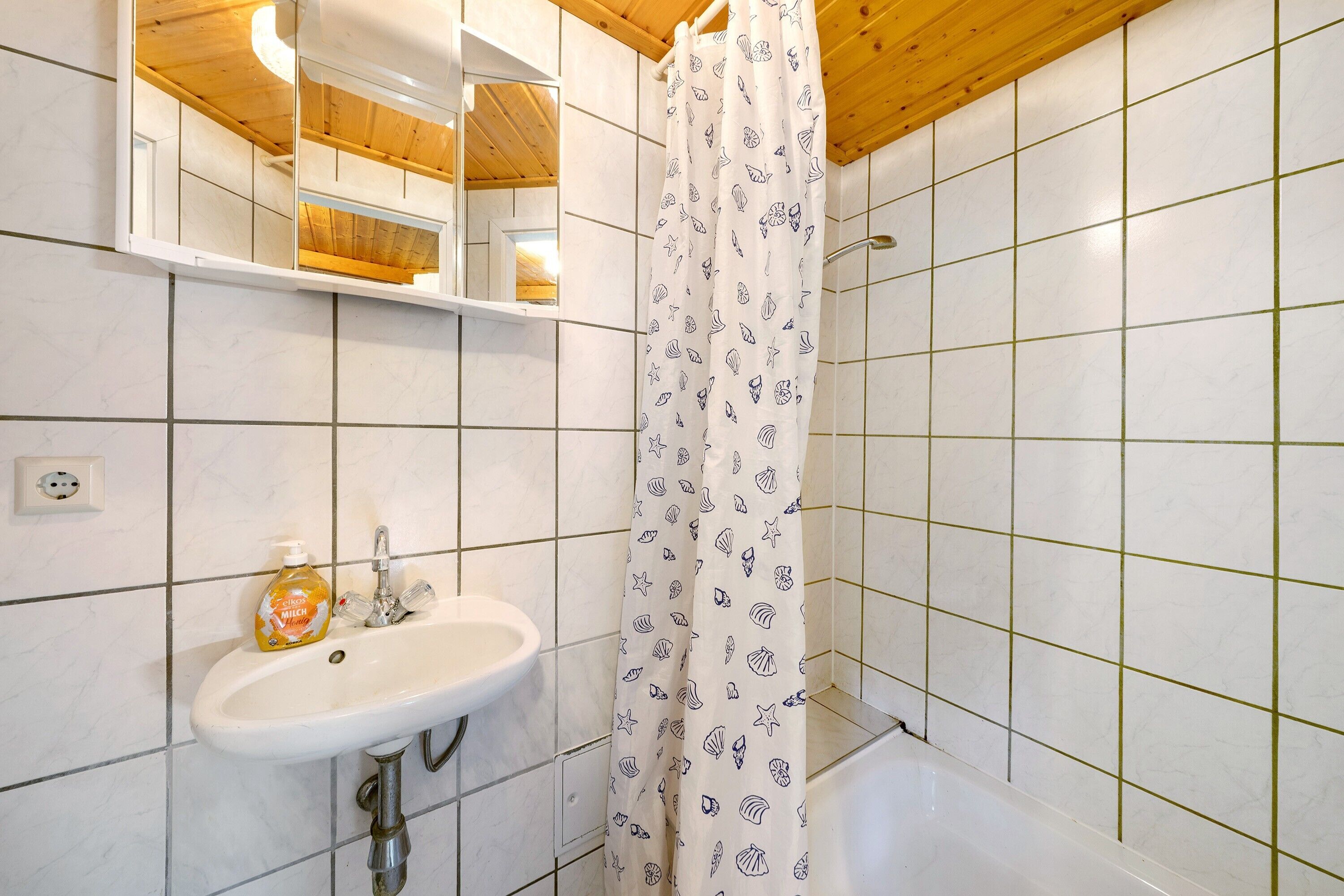 Ein Badezimmer mit einem weißen Waschbecken, einem Spiegel, einem Duschvorhang mit Meeresmuschelmuster und einer Badewanne.