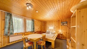 Interior de una cabaña de madera con una mesa de comedor, sillas, una cama y un radiador.
