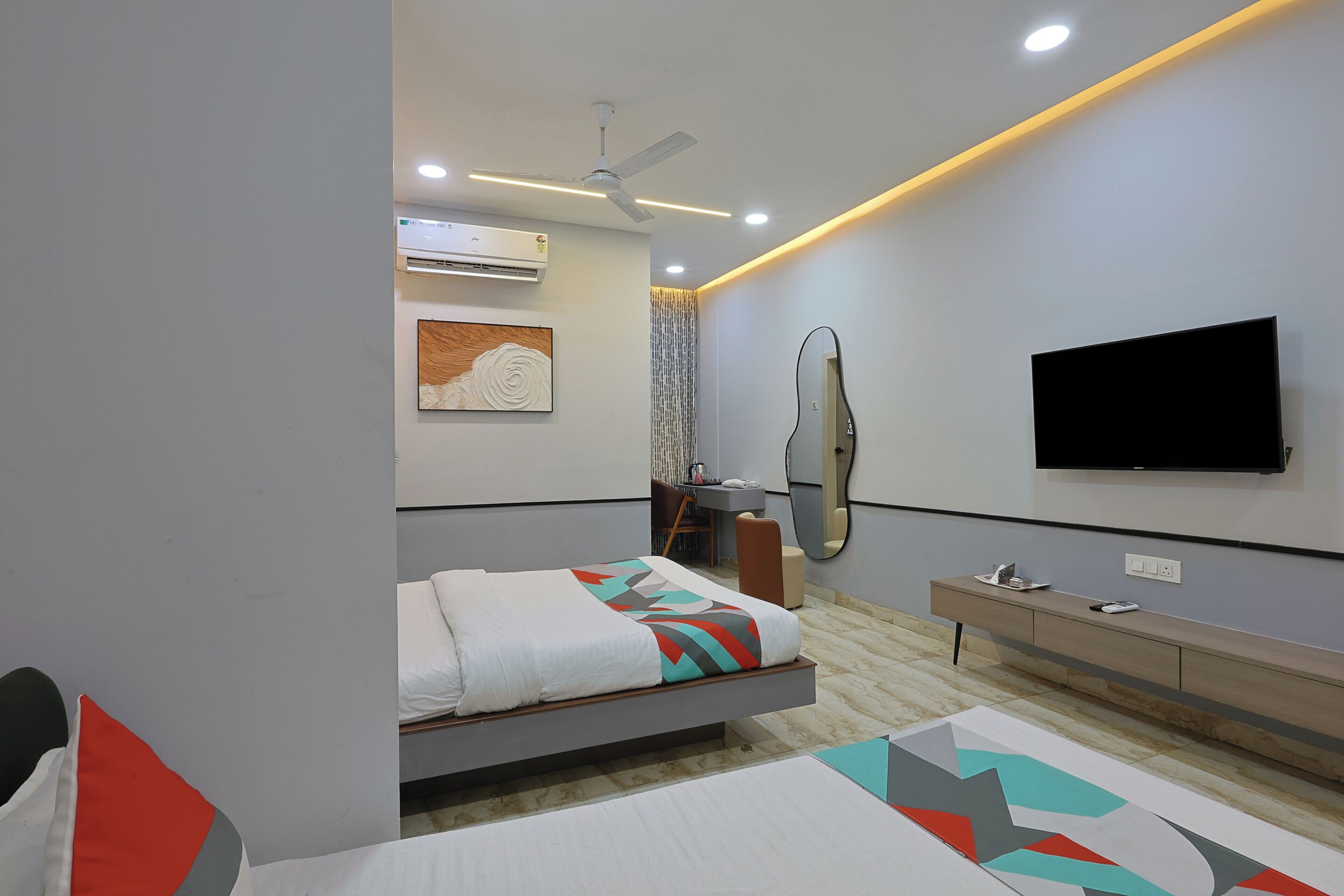 A modern bedroom with a bed, bedside table, TV, and a mirror.