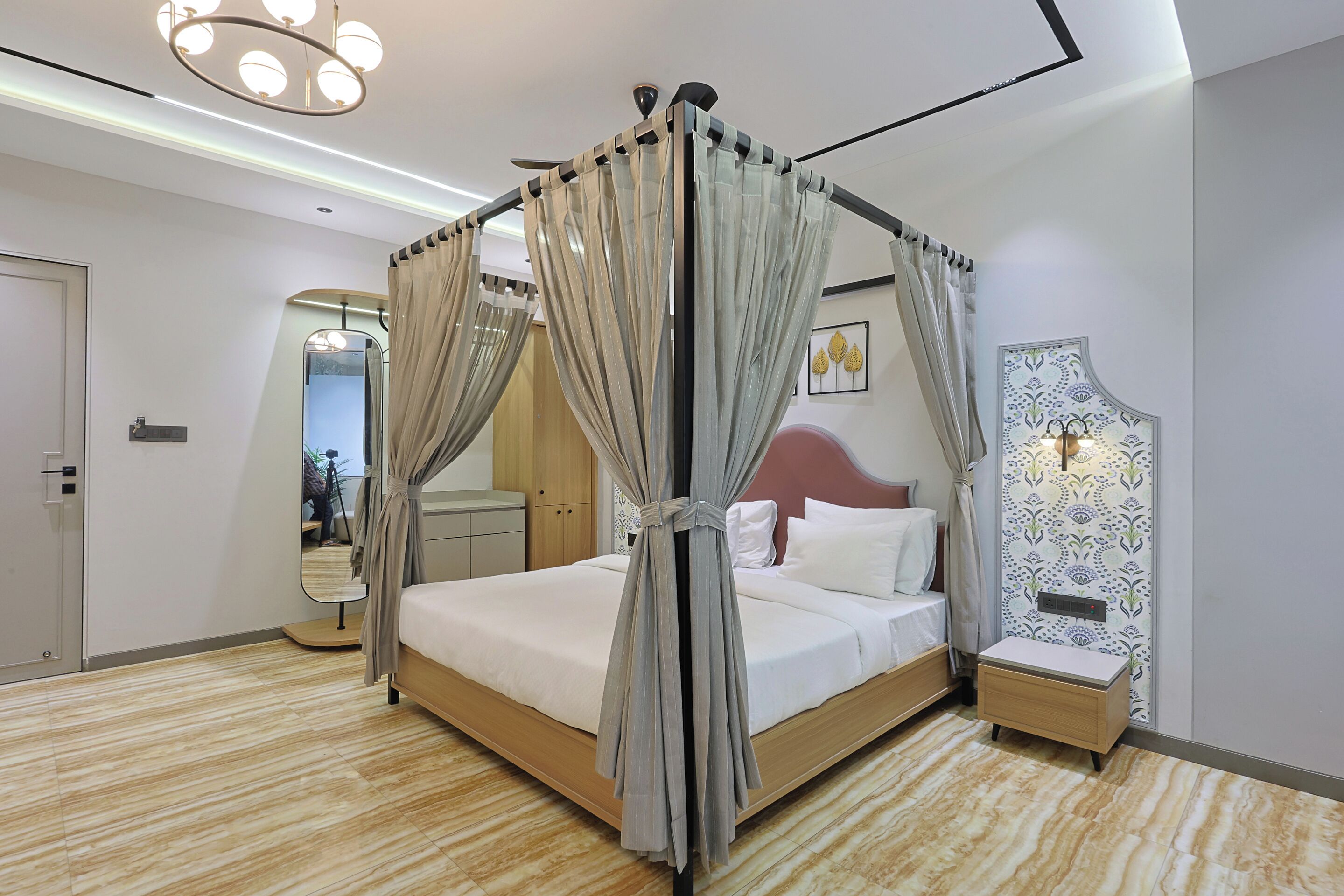 A modern bedroom with a four-poster bed, a bedside table, a nightstand, a mirror, and a wall-mounted light fixture.