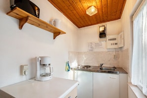 Une cuisine compacte équipée d’une machine à café, d’une cuisinière intégrée et d’un luminaire en bois au plafond.